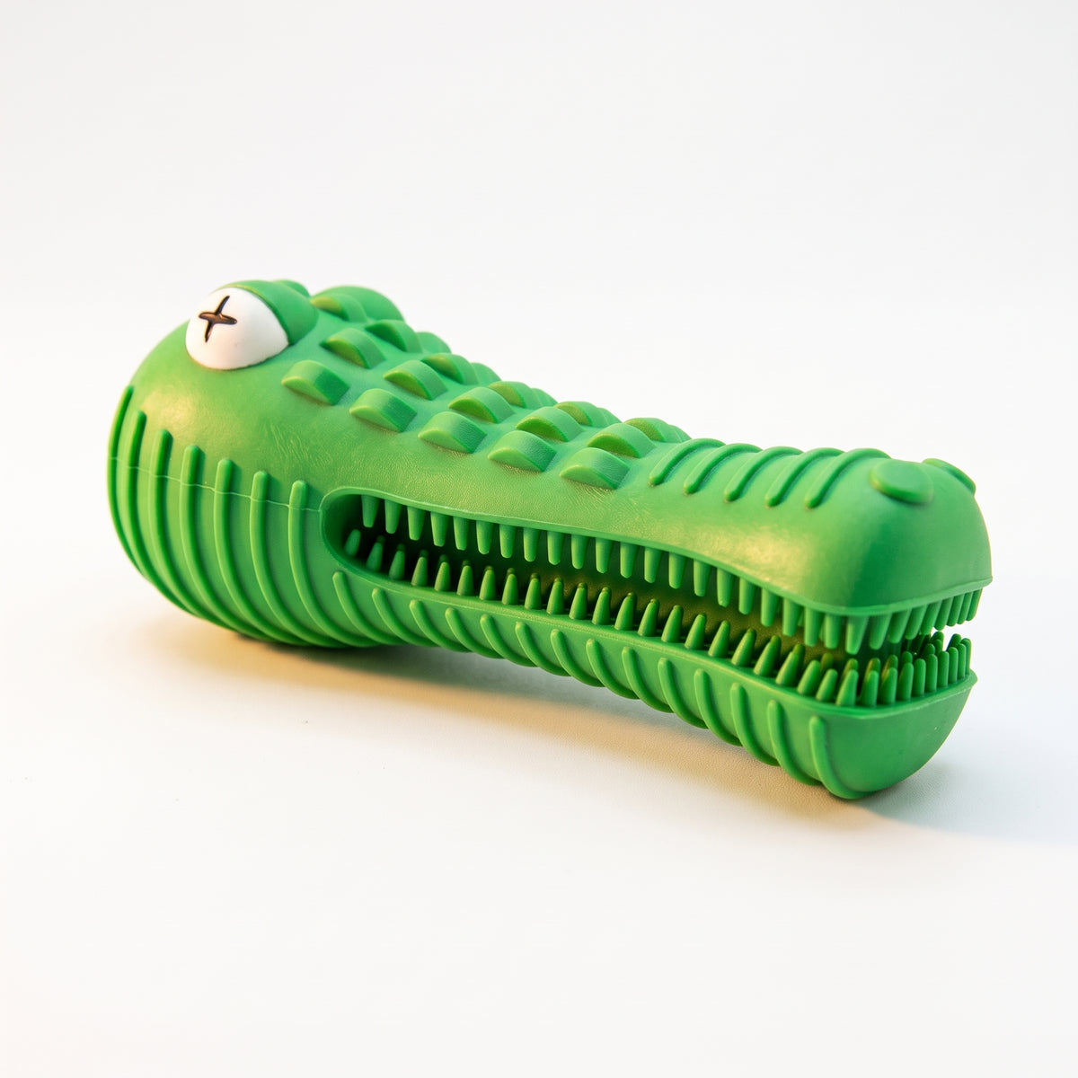 A green crocodile-shaped silicone product with a ribbed textured body, open mouth with teeth, and a white eye with a black X, photographed on a clean white background.