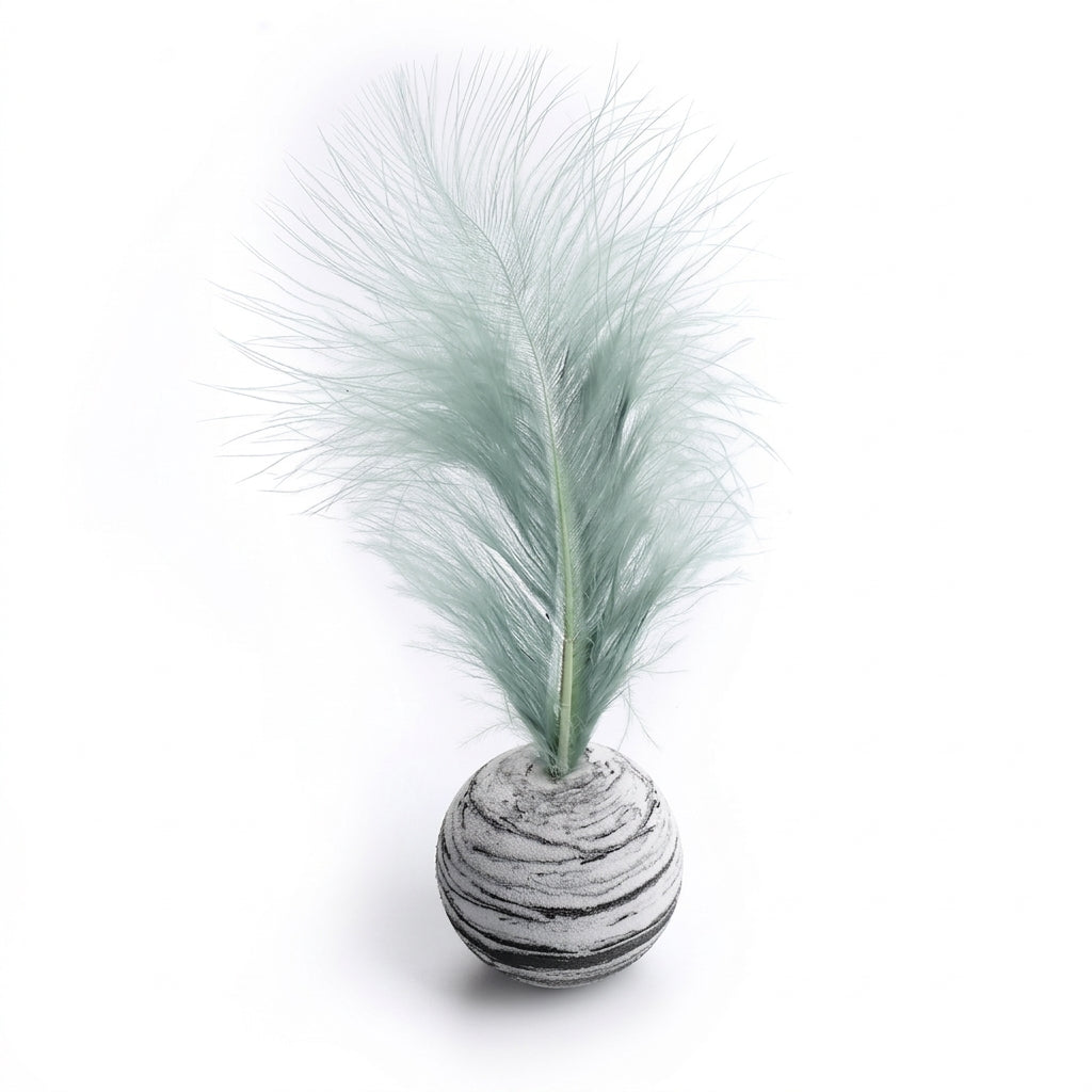 A decorative tabletop piece featuring a pale mint green pampas-style feather mounted on a round, horizontally striped gray and white base, shown on a clean white background.