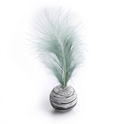 A decorative tabletop piece featuring a pale mint green pampas-style feather mounted on a round, horizontally striped gray and white base, shown on a clean white background.