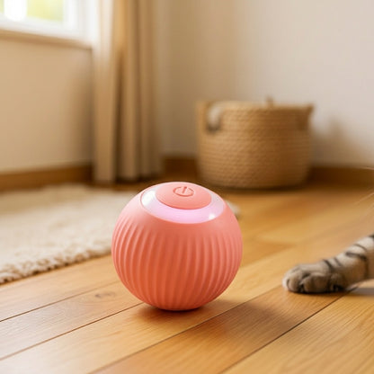 A pink ribbed spherical pet toy sits on a wooden floor in a softly lit room, with a cat's paw visible at the right edge.